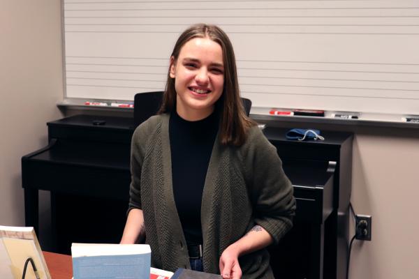 Heidi Bowles sitting at desk with books and piano in the background